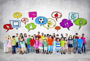 Diverse children stand by gray wall under colorful speech bubbles showing global ideas and learning symbols.